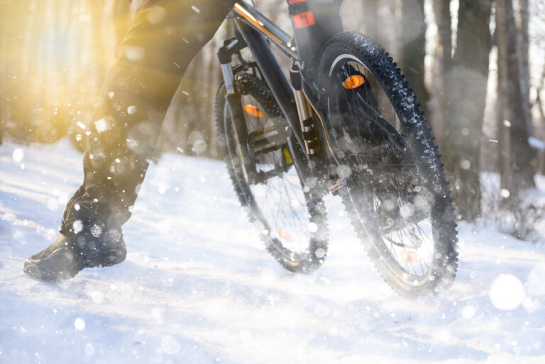 Professional Cyclist Riding the Bike on the Snowy Trail Lit by the Sun. Winter Extreme Sports Concept.