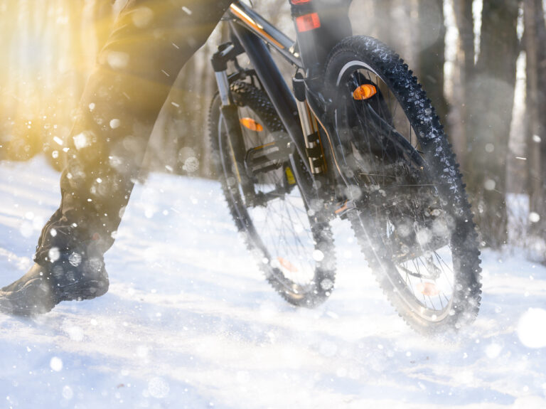 Professional Cyclist Riding the Bike on the Snowy Trail Lit by the Sun. Winter Extreme Sports Concept.